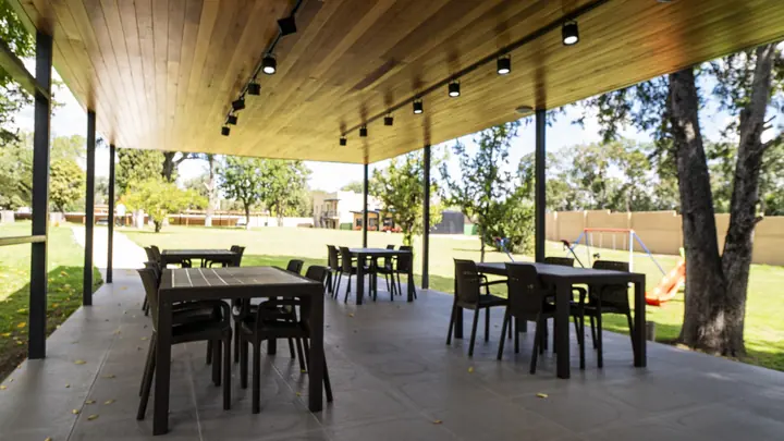Galería y quincho con mesas bajo los árboles